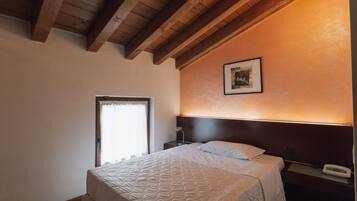 Una habitación de hotel con cama, mesita de noche, un cuadro enmarcado en la pared y una ventana con cortinas.