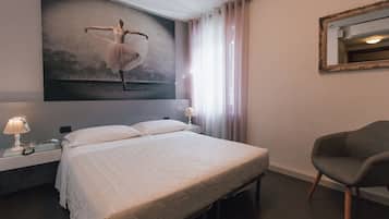 A hotel room with a large bed, a nightstand with a lamp, a chair, a wall-mounted mirror, and a ballet dancer painting.