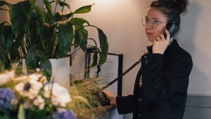 Una persona está de pie en la recepción, con una planta y flores en un jarrón.