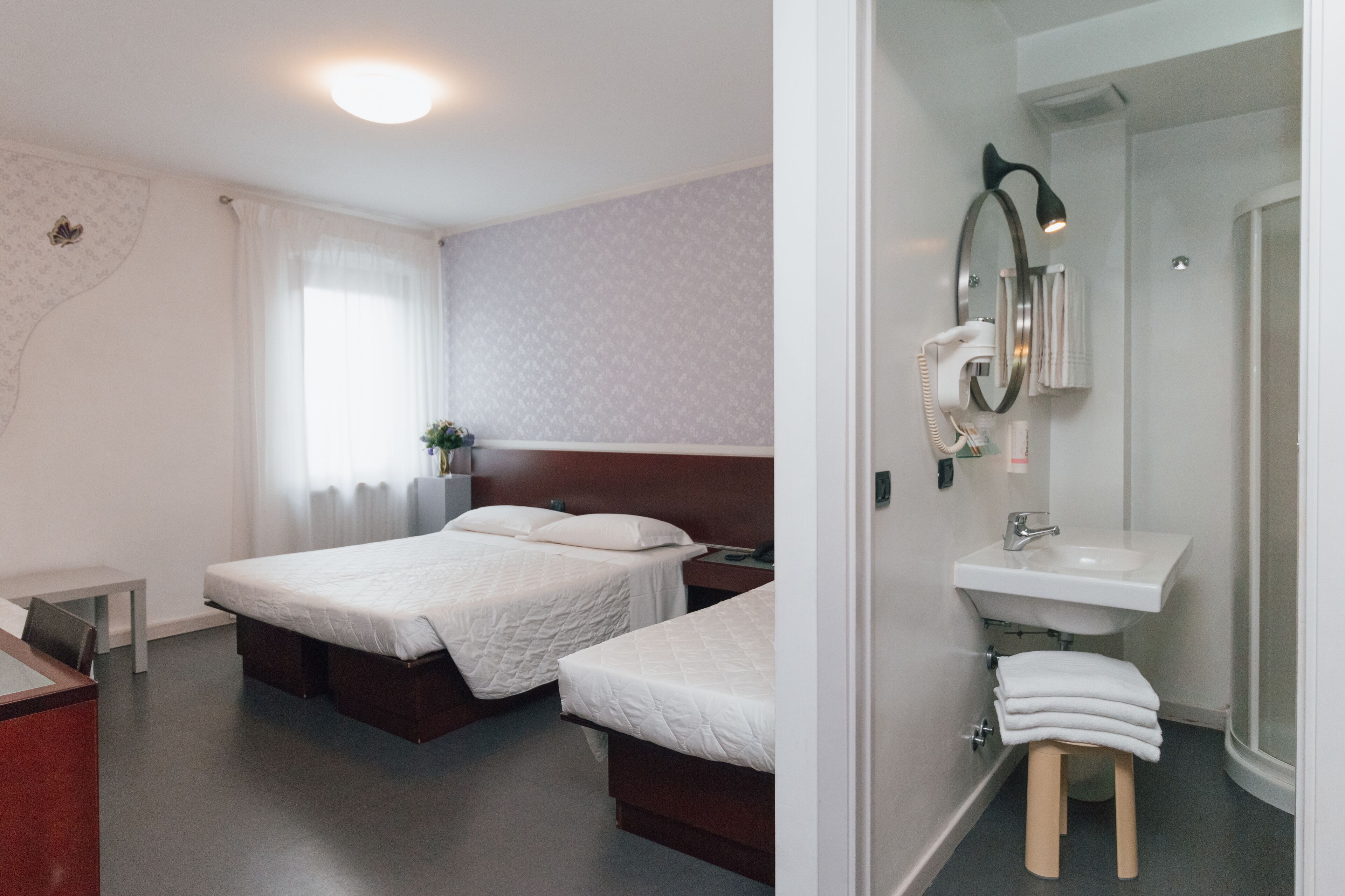 A hotel room with two beds, a desk, a small table, a shower, and a sink.
