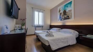 Een hotelkamer met twee bedden, een bureau met een computer, een aan de muur bevestigde televisie en een schilderij boven het bed.