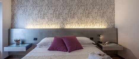 A hotel room with a large bed, a headboard with a tree pattern, a bedside table with a lamp, and a nightstand with a phone and a mouse.