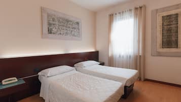 A hotel room with two beds, a bedside table with a phone, a wall-mounted artwork, and a window with curtains.