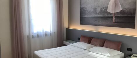 A bedroom with a large bed, a nightstand, a wall-mounted phone, and a window with curtains.