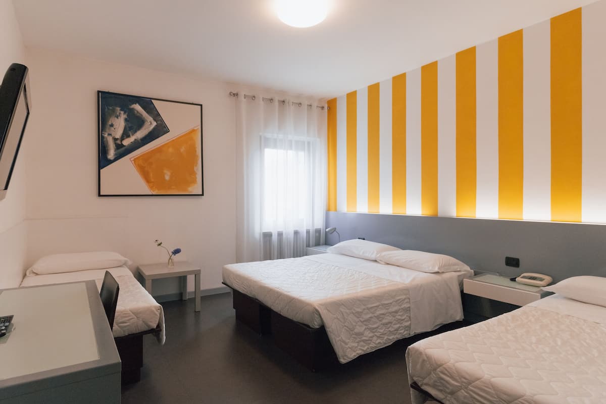 Ett hotellrum med två sängar, ett skrivbord, en stol, ett sängbord och en tavla på väggen.