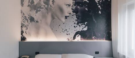 Une chambre avec un grand tableau abstrait au mur, un lit recouvert de draps blancs, une table de chevet avec une lampe et une fenêtre avec des rideaux.