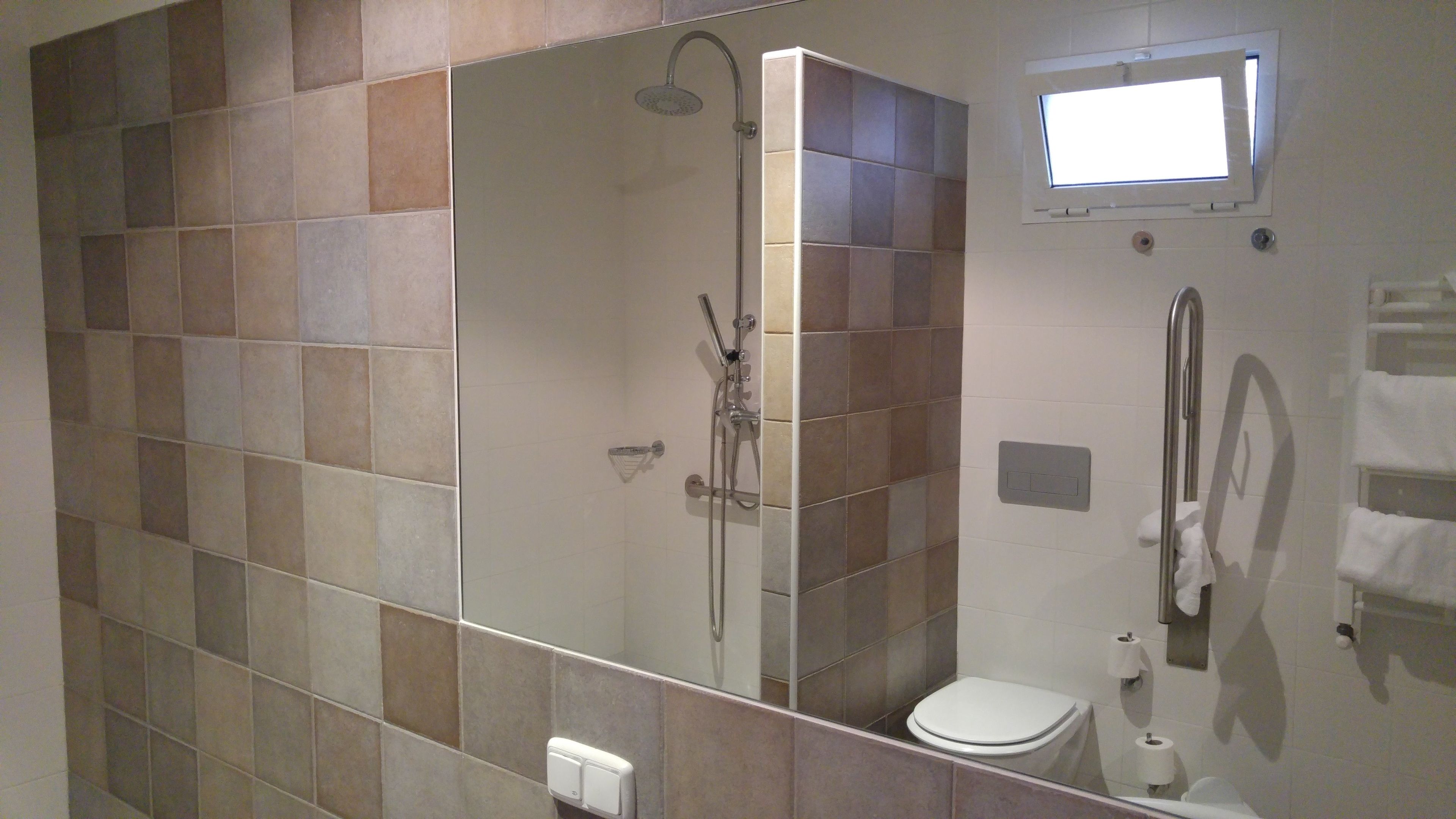 Un baño moderno con ducha acristalada, inodoro y una ventana pequeña.