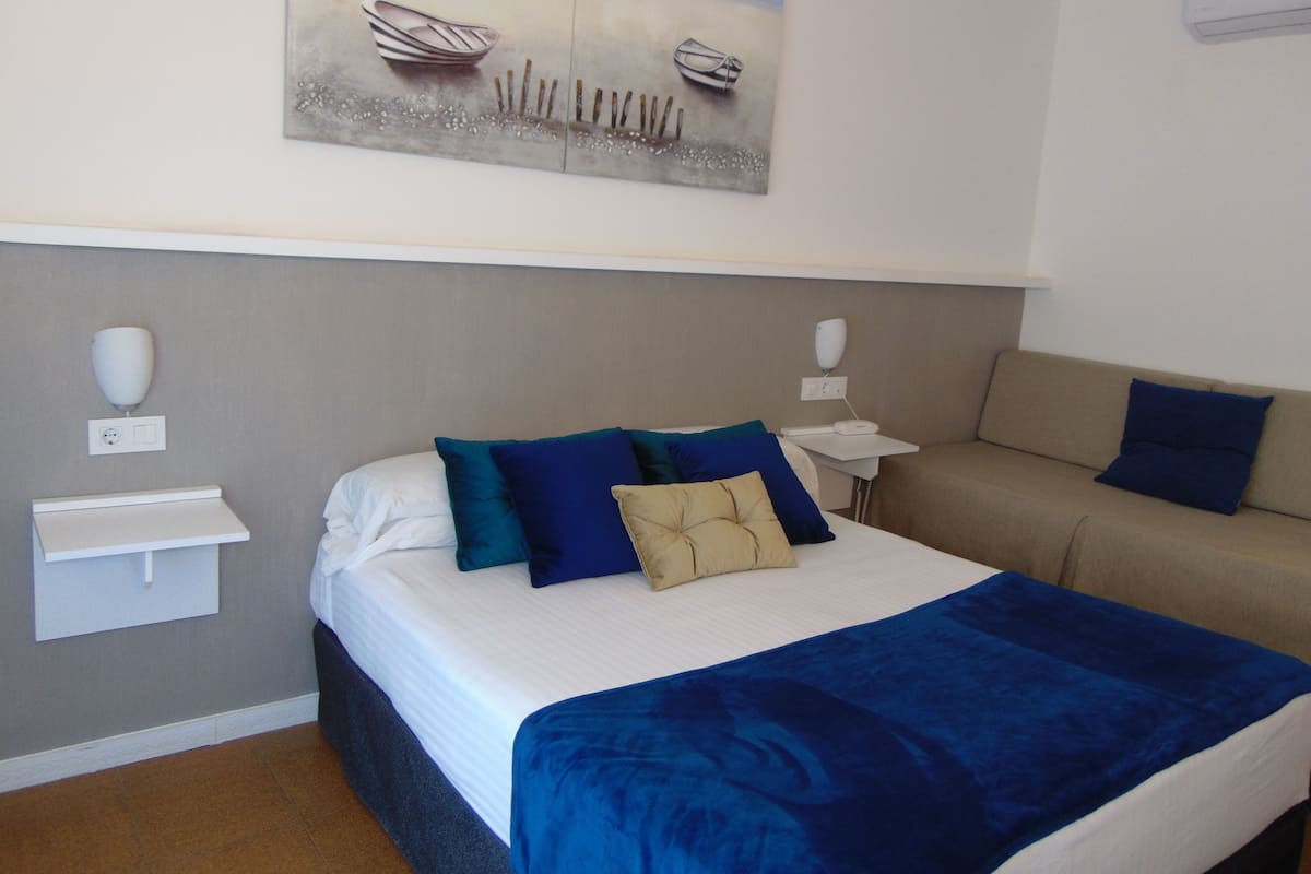 Habitación de hotel con cama, mesita de noche, sofá y un cuadro en la pared.