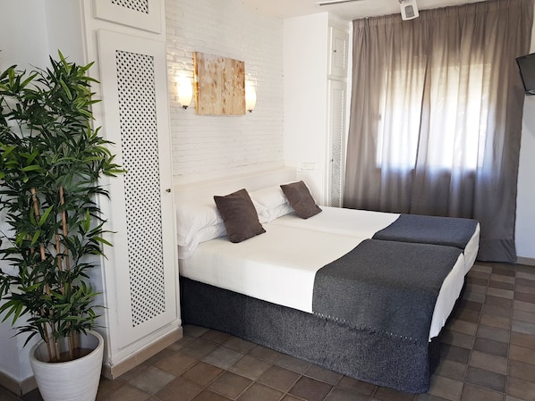 Habitación de hotel con cama, una planta en maceta, una obra de arte en la pared y ventana con cortinas.