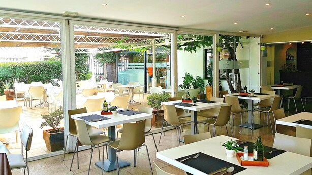 An indoor/outdoor dining area with tables and chairs, potted plants, and a view of the outside. - Hotel Campomar Playa (El Puerto de Santa Maria)