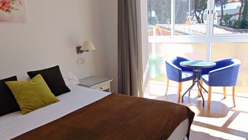 Quarto de hotel com cama, uma mesinha com duas cadeiras, abajur e vista para o exterior.