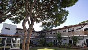 A courtyard with a large tree, a building with multiple floors, and potted plants. - Hotel Campomar Playa (El Puerto de Santa Maria)