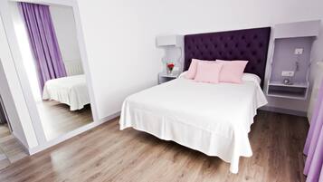 Una habitación de hotel moderna con una cama grande, una mesita de noche, un espejo y un cabecero morado.