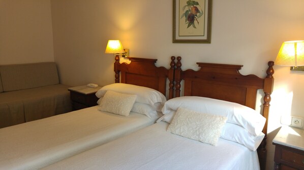 Habitación de hotel con dos camas individuales, cabecera de madera, lámparas de noche, mesitas de noche y un sofá.