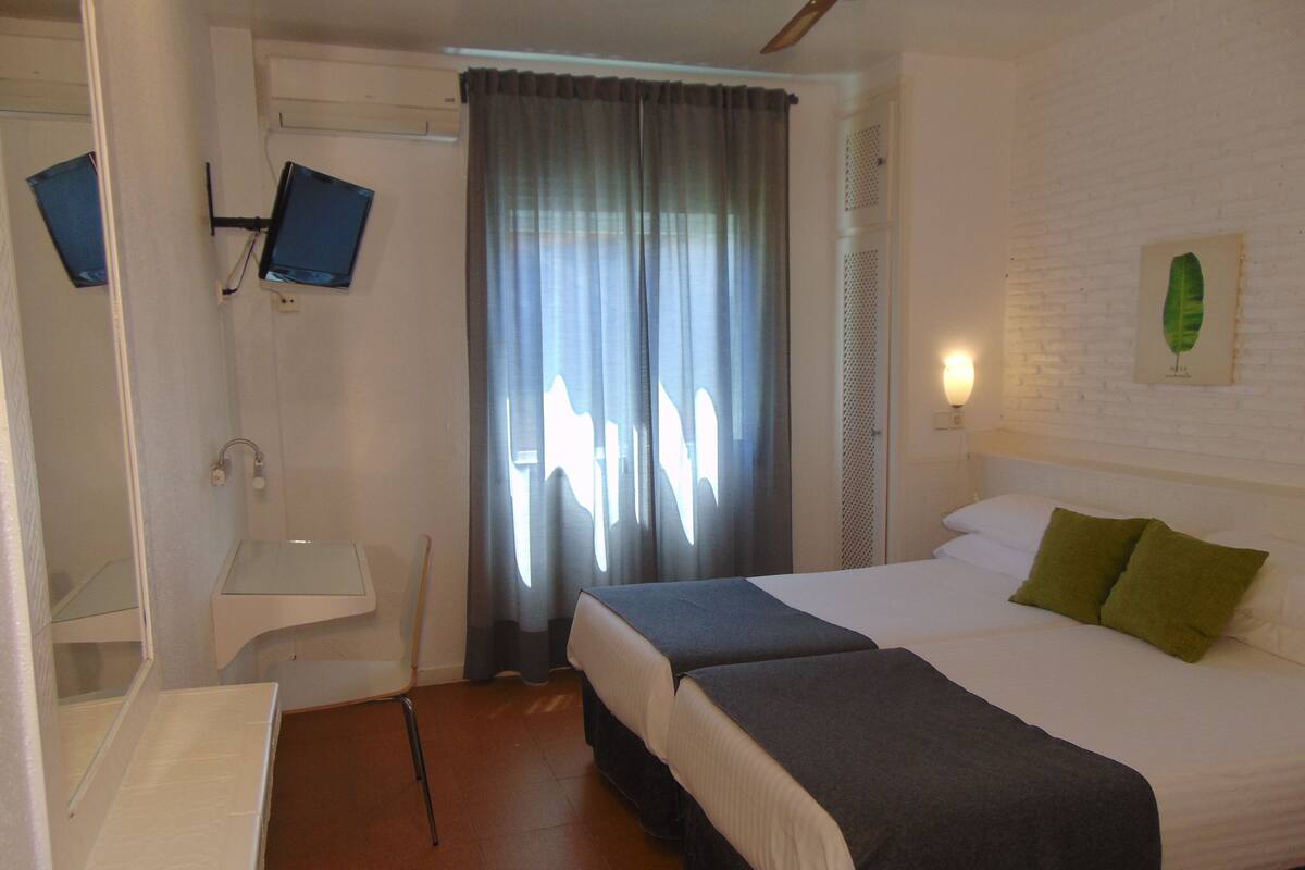 Una habitación de hotel con una cama, dos mesitas de noche, un espejo, ducha y cortina.