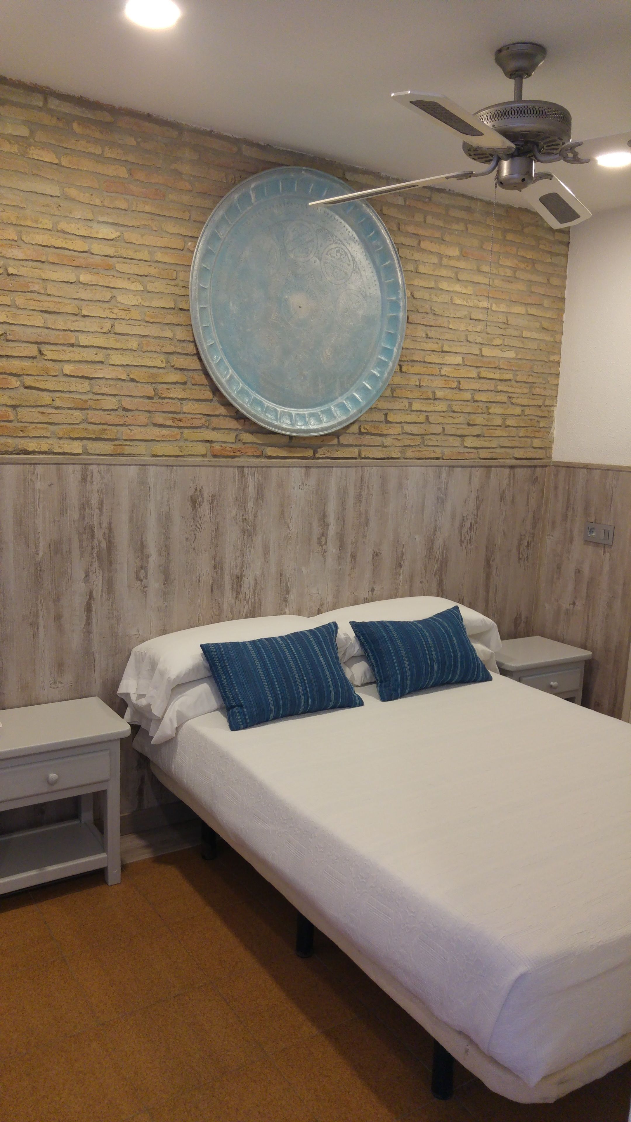 A bedroom with a bed, two nightstands, a round wall decoration, a ceiling fan, and a wooden headboard.
