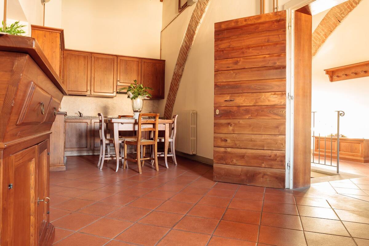 A kitchen with wooden cabinets, a dining table with chairs, and a large wooden door.