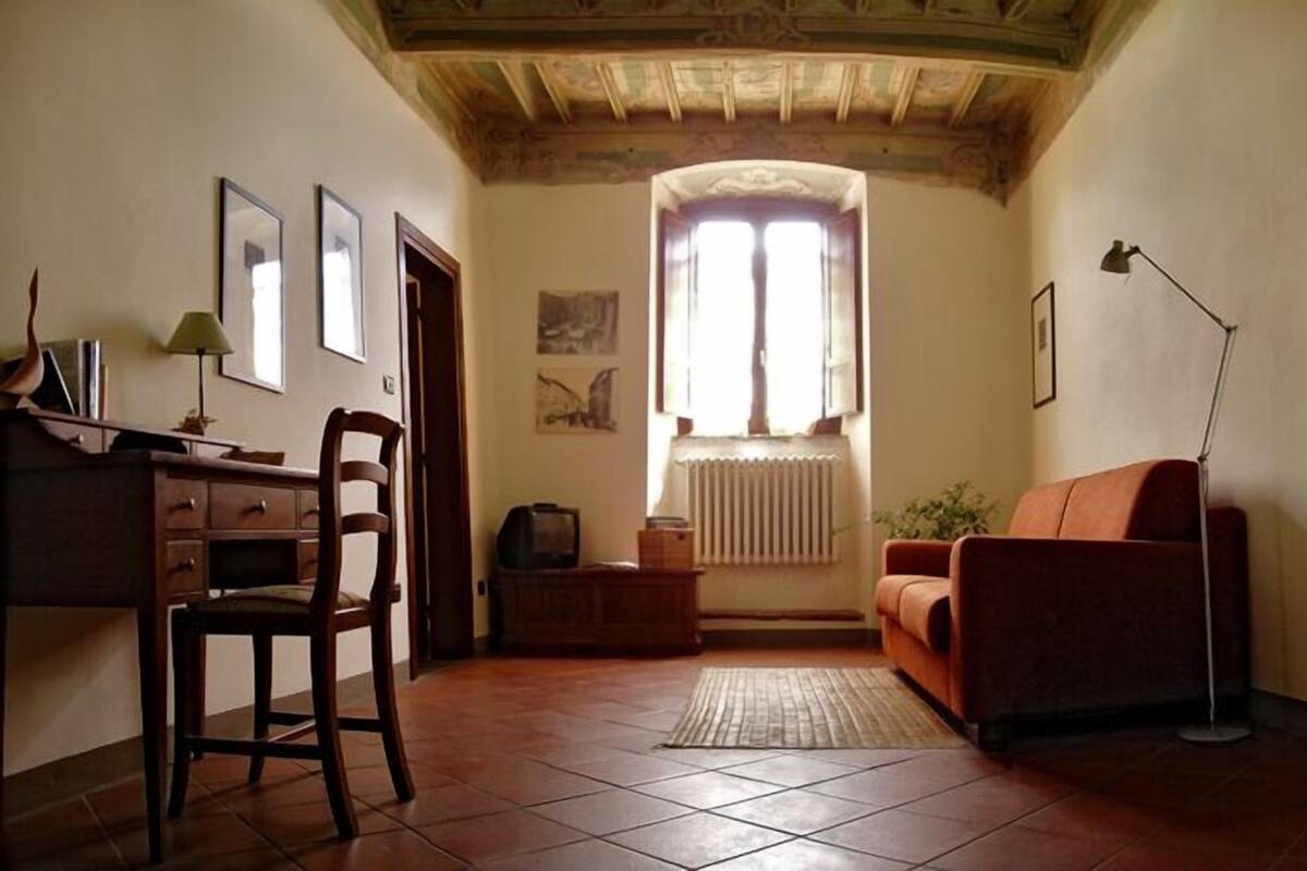 A cozy living room with a wooden desk, a chair, a sofa, and a radiator.