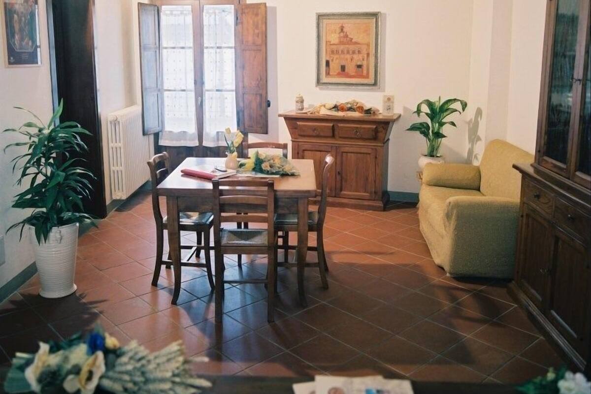 A dining area with a wooden table and chairs, a yellow armchair, a cabinet, and a potted plant.