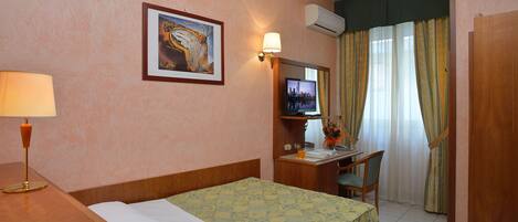 Habitación de hotel con cama, escritorio, silla, televisor y lámpara.