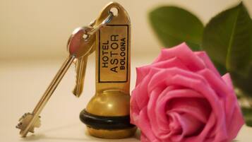 Une clé avec une étiquette d’hôtel indiquant « HÔTEL ASTOR BOLOGNE » et une rose rose.