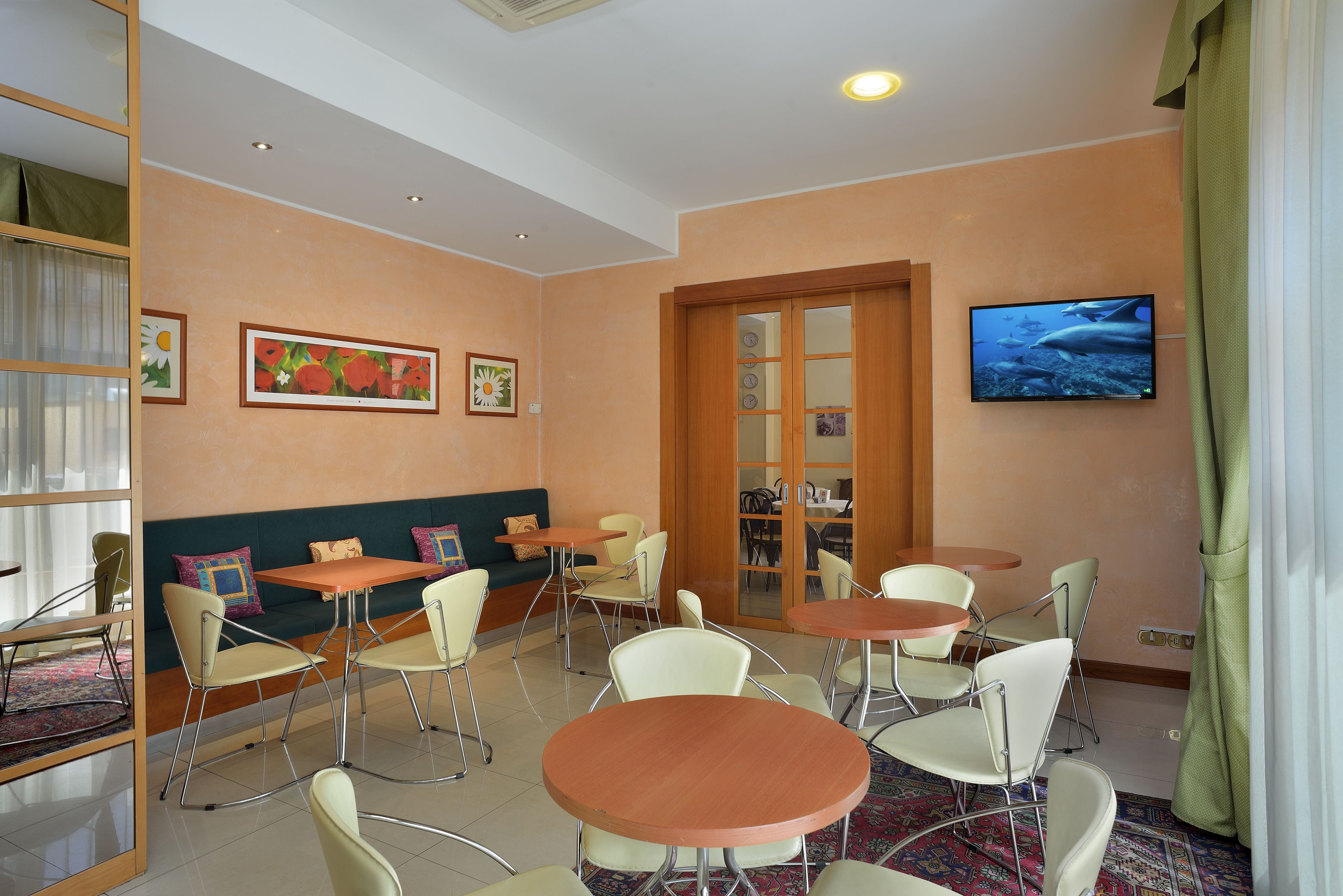 A hotel room with a sofa, two tables, and chairs. There is a television on the wall and a window with curtains.
