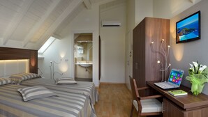 A modern bedroom with a large bed, bedside tables, a desk with a laptop, and a TV on the wall. - Hotel Astor (Bologna)