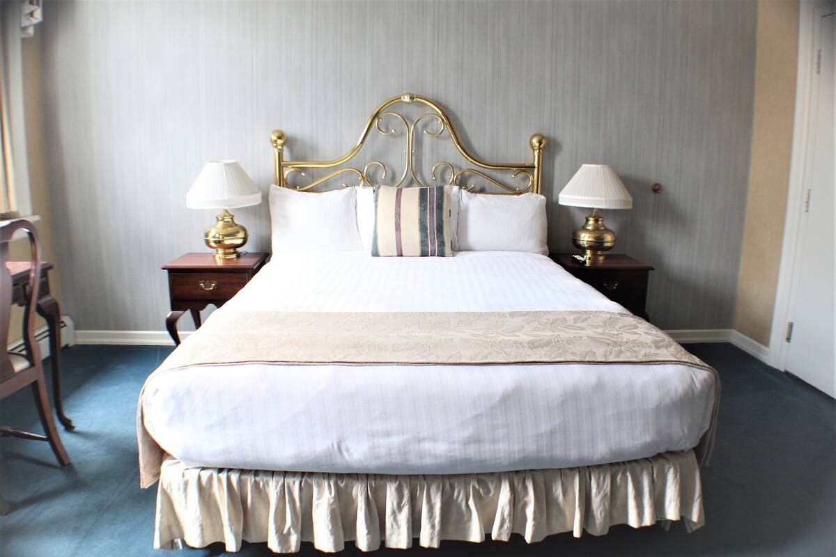 A neatly made bed with a gold headboard, two bedside tables with lamps, and a chair to the left.