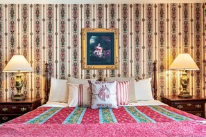 A bed with a patterned quilt, a pillow with 'Walker Farms' text, and a framed painting above.