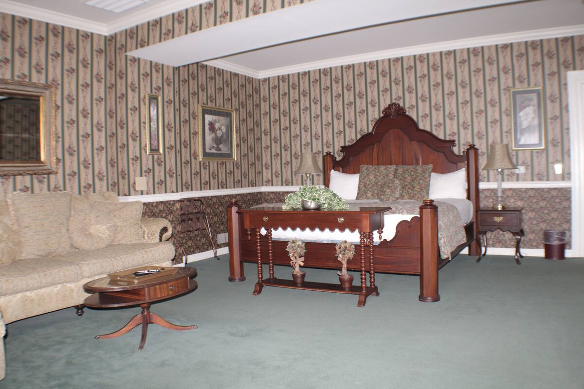 A bedroom with a large bed, a wooden nightstand, a round coffee table, and a sofa.