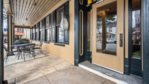 An outdoor seating area with tables and chairs, a covered walkway with a slatted ceiling, and a building entrance with a glass door. - Waynebrook Inn, Est 1865 (Honey Brook)