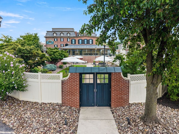 A brick building with a green roof, a white fence, and a tree in the foreground.
