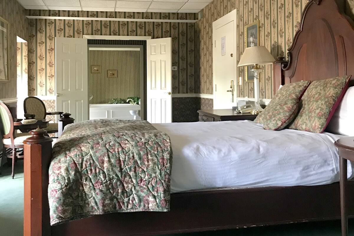 A bedroom with a bed, a nightstand, a mirror, a dresser, and a chair.