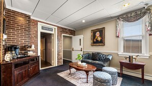 A cozy living room with a coffee bar, a leather sofa, ottomans, and a framed portrait on the wall. - Waynebrook Inn, Est 1865 (Honey Brook)