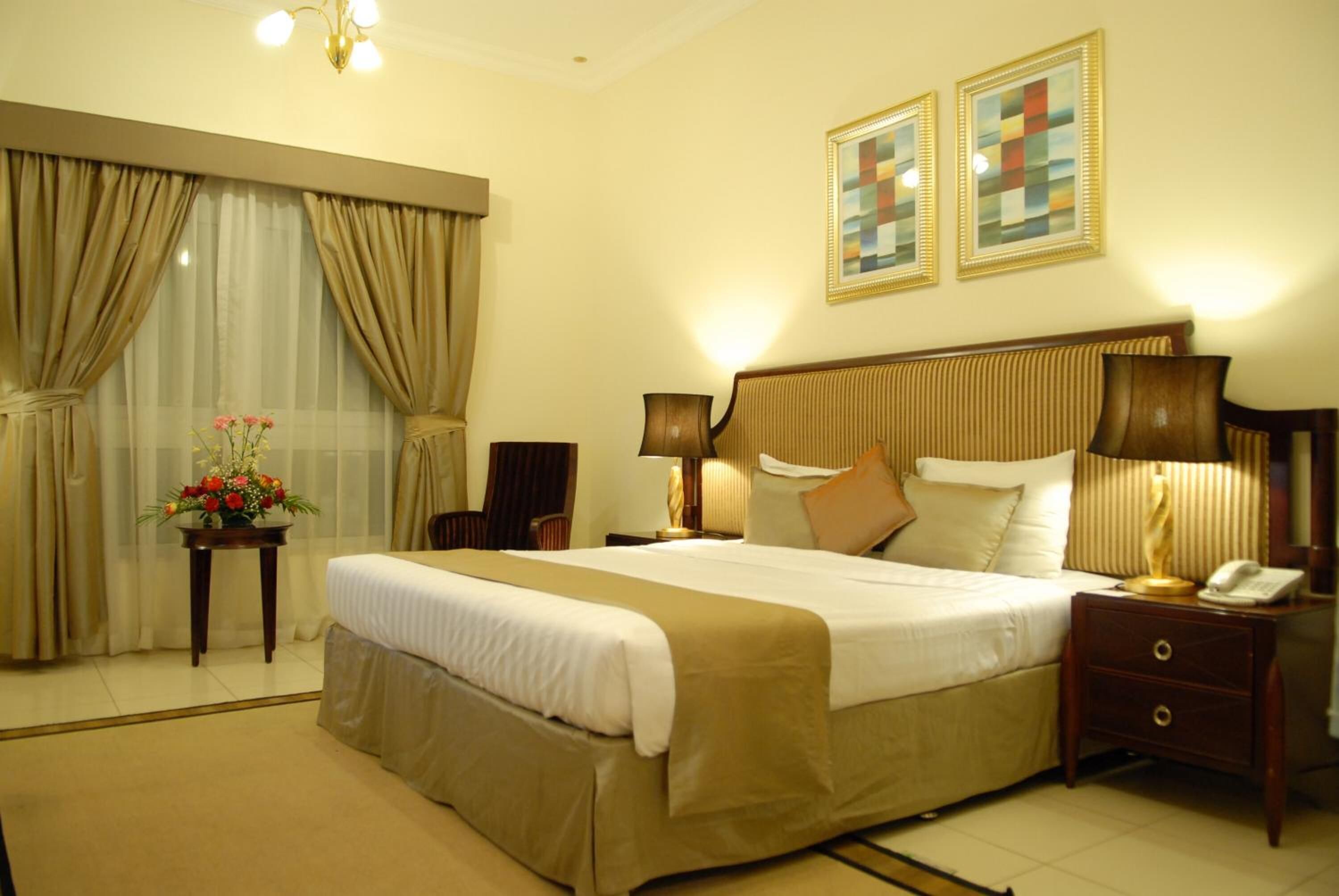 A hotel room with a large bed, two bedside lamps, a nightstand with a phone, and a window with curtains.
