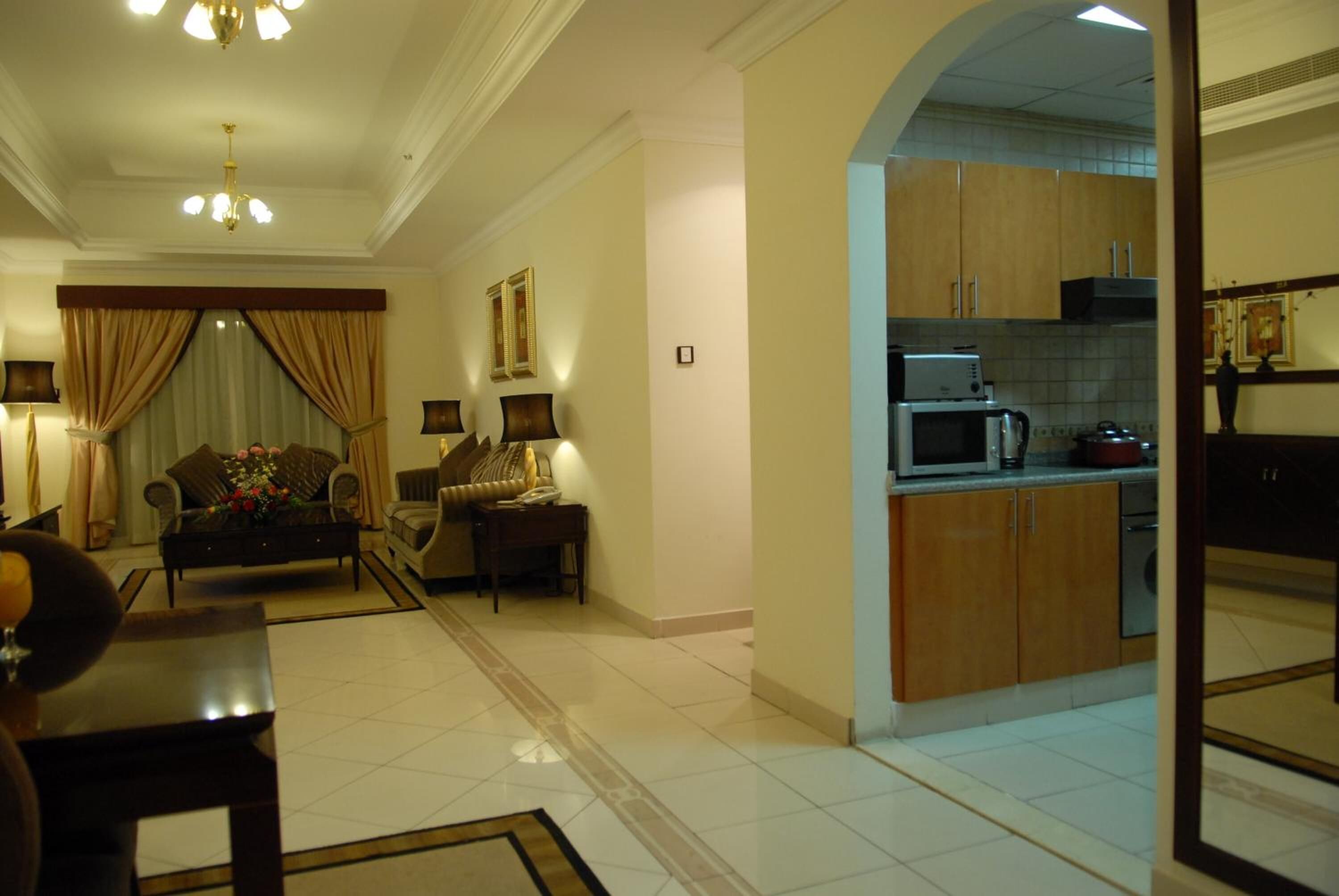 A hotel room with a living area, a sofa set, a dining table, and a kitchen area with modern appliances.