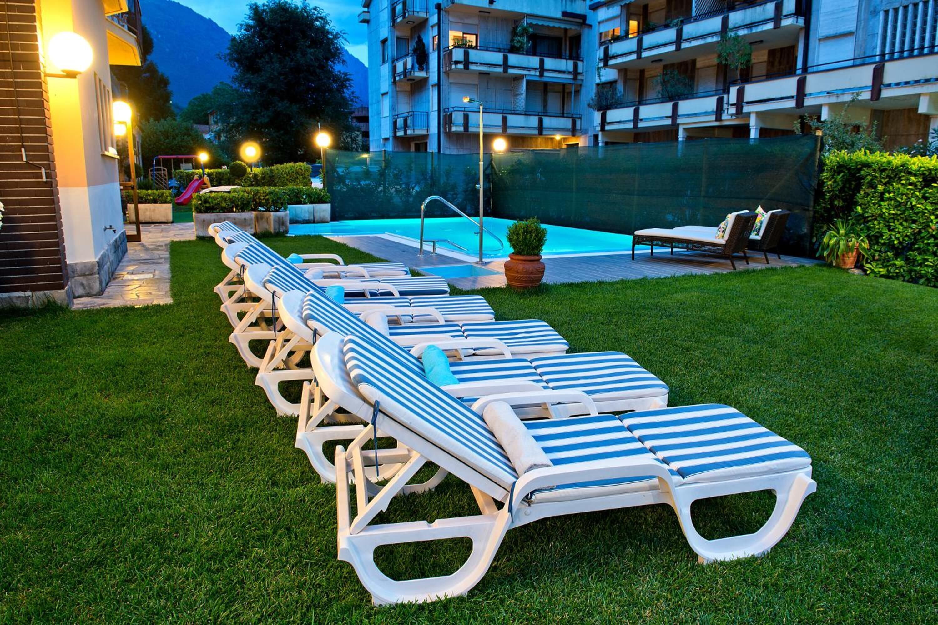 Zona junto a la piscina con sillas de descanso y una piscina, rodeada de un césped cuidado y un edificio al fondo.