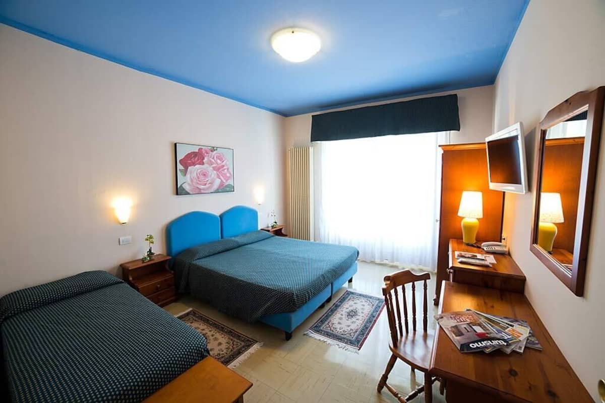 A hotel room with two beds, a desk, a chair, a TV, and a painting on the wall.