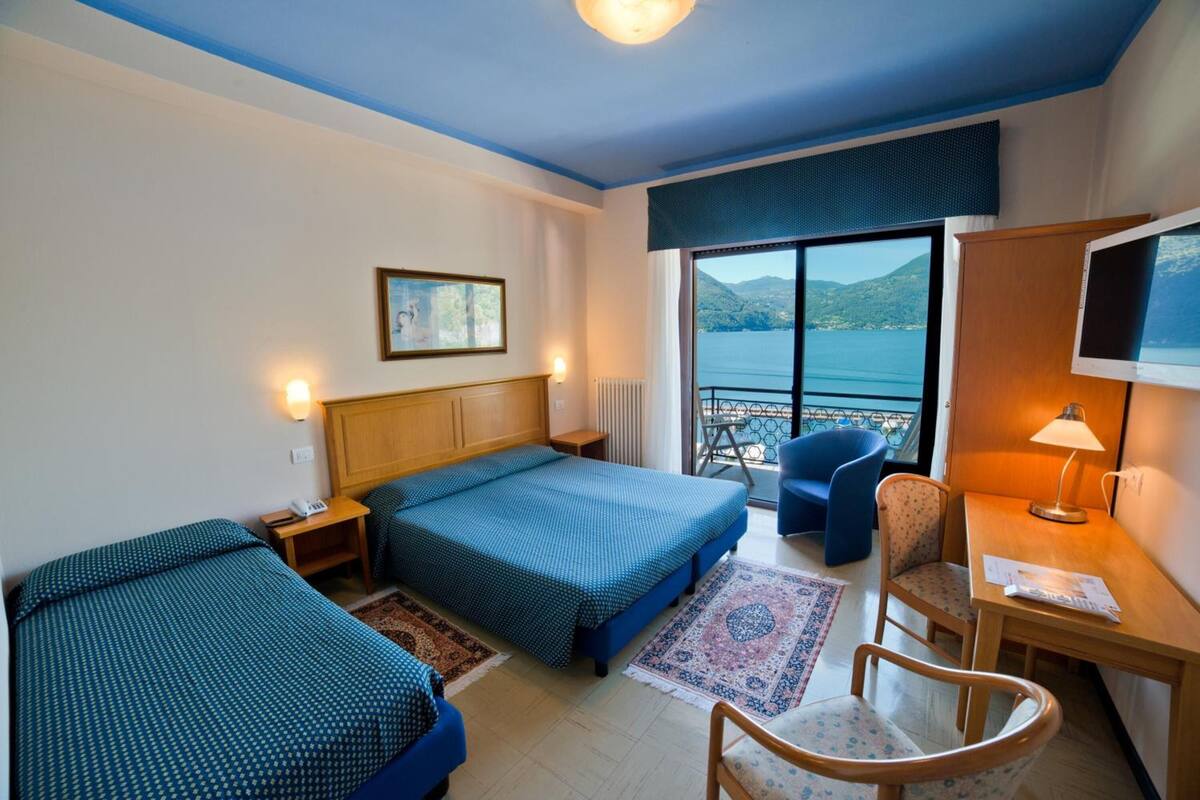 A hotel room with two beds, a desk, a chair, a TV, and a view of the sea.