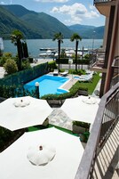 A pool area with lounge chairs and umbrellas, overlooking a body of water and mountains.