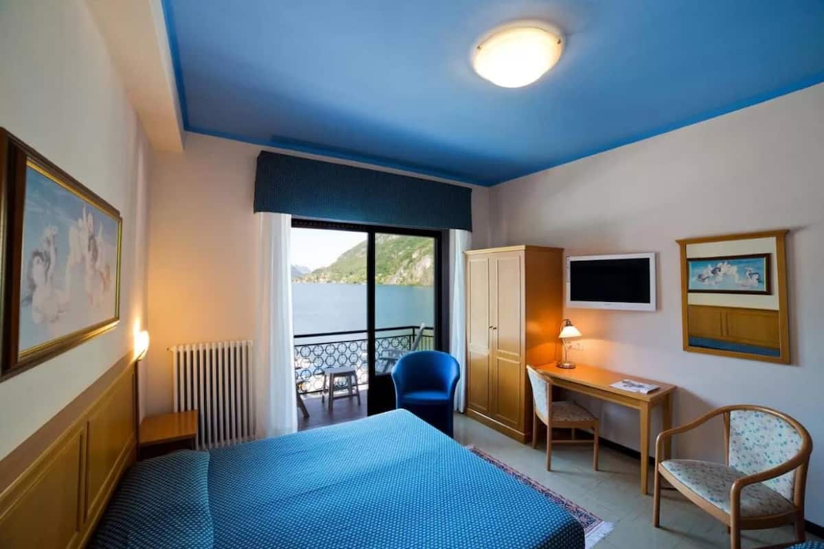 A hotel room with a bed, a desk, a chair, a TV, and a view of the outdoors.