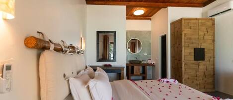A bedroom with a wooden ceiling, a bed with white bedding, a bedside table, and a mirror on the wall.