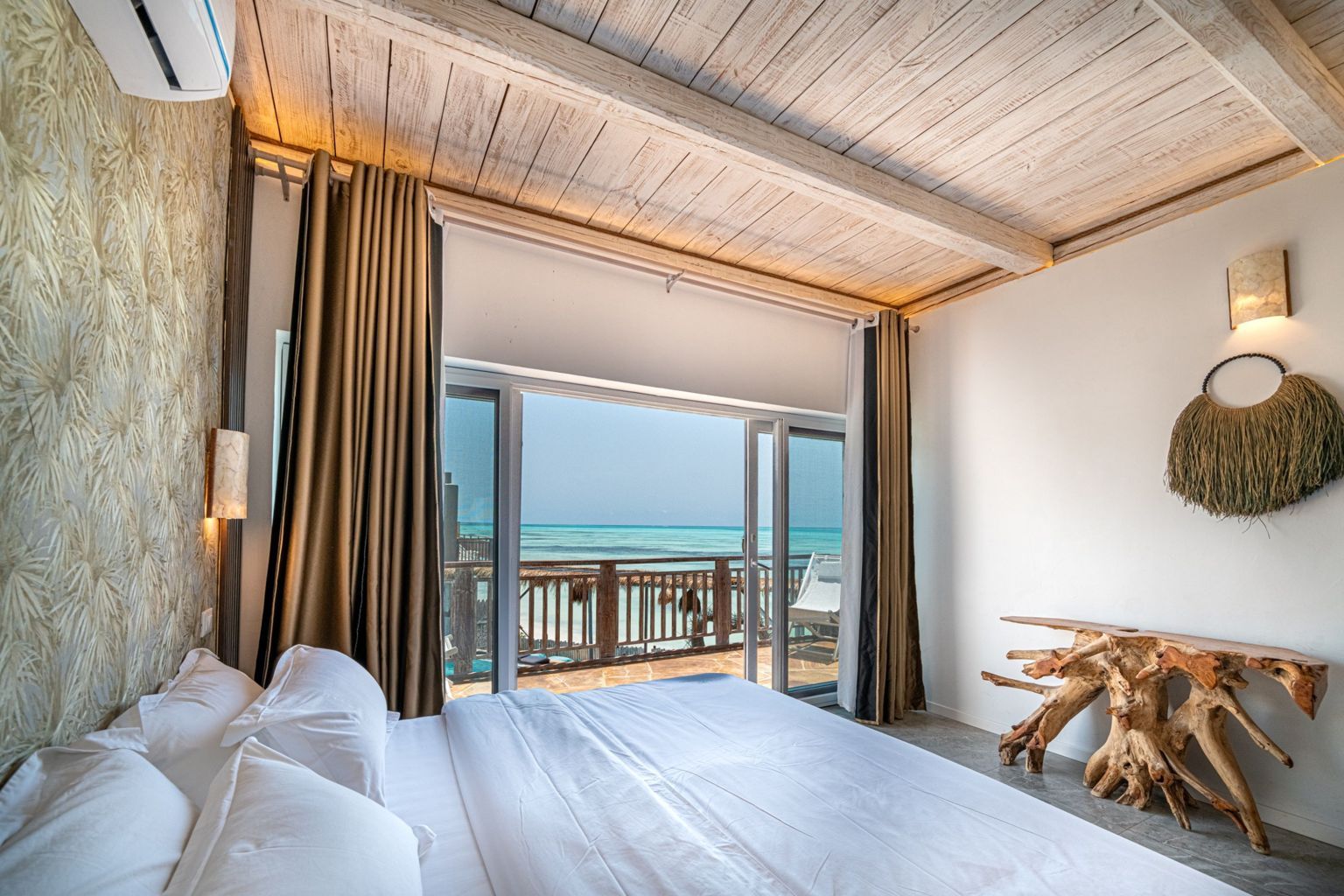 Una camera d'hotel con un letto grande, vista sulla spiaggia e soffitto in legno.