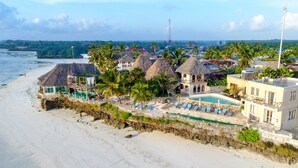 Un hôtel situé en bord de mer, doté d’une piscine, de bâtiments à toits de chaume et d’une plage de sable.