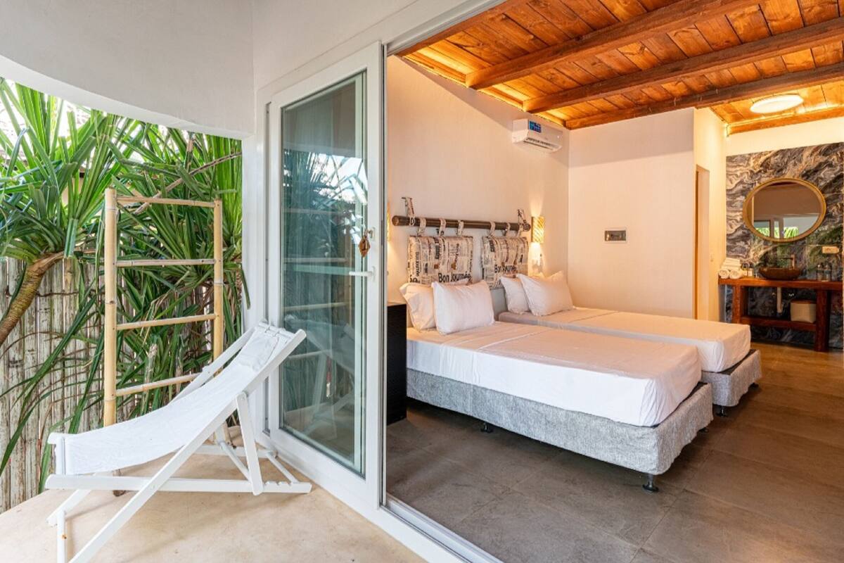 Une chambre avec deux lits, une porte vitrée donnant sur un balcon et un plafond en bois.
