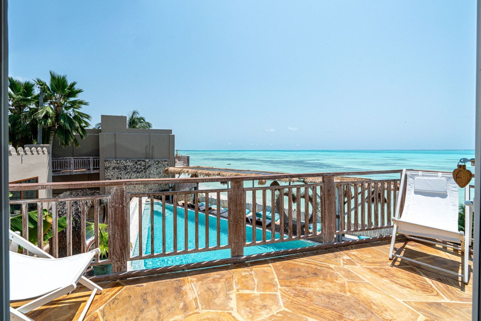 A pool area with a wooden deck, lounge chairs, and a view of the ocean.
