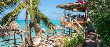 A beachside resort with thatched-roof structures, wooden seating, and lush greenery.