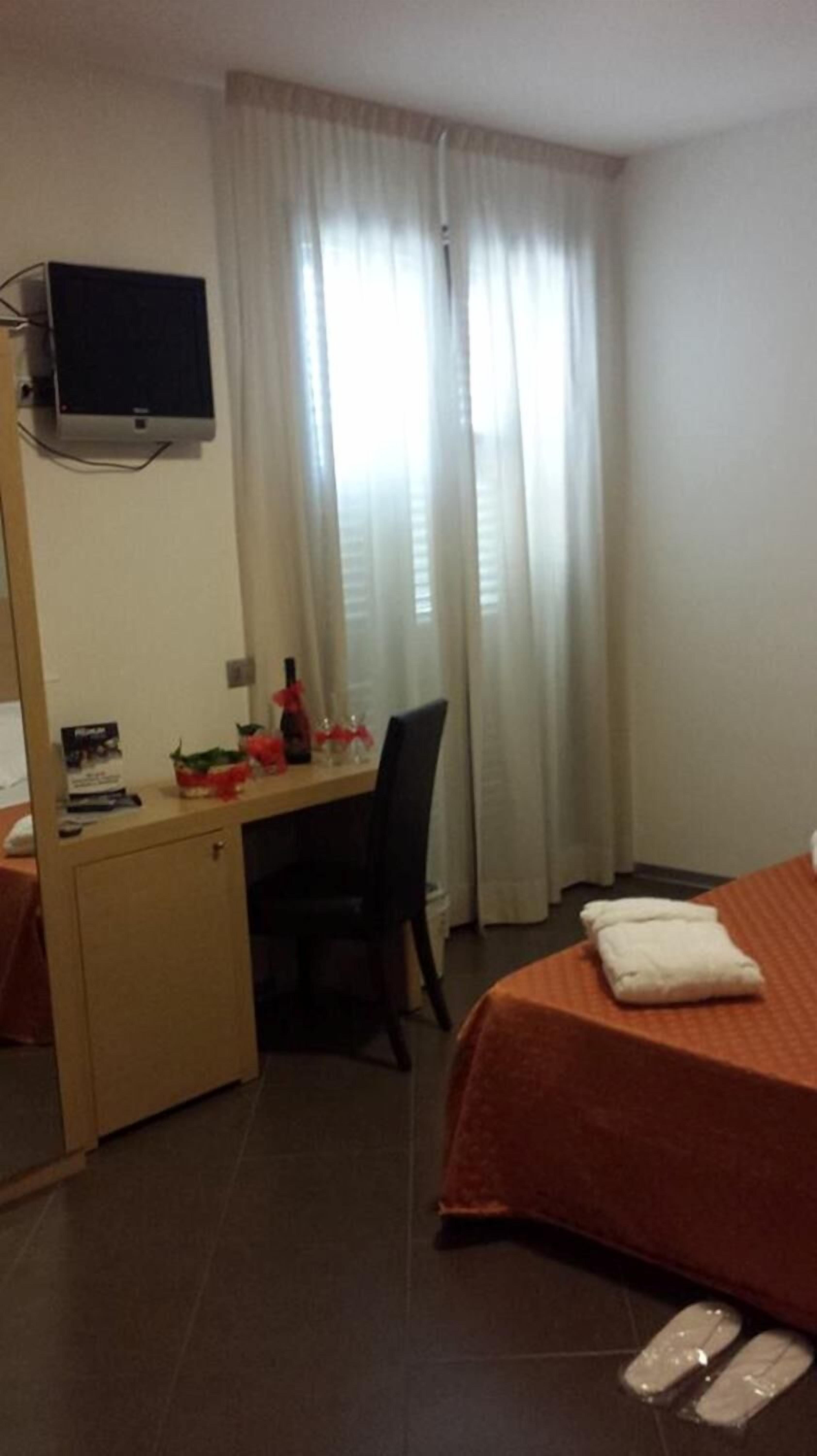 Una camera d'albergo con un letto, una scrivania, una sedia, una televisione e una finestra con tende.