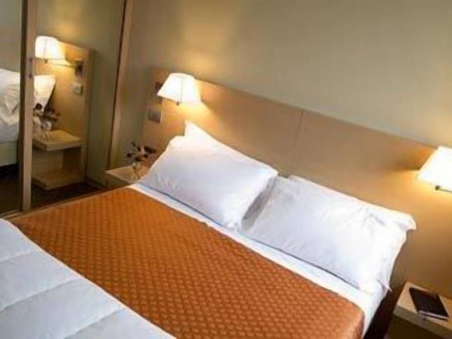 A hotel room with a large bed, two bedside lamps, and a nightstand with a lamp.