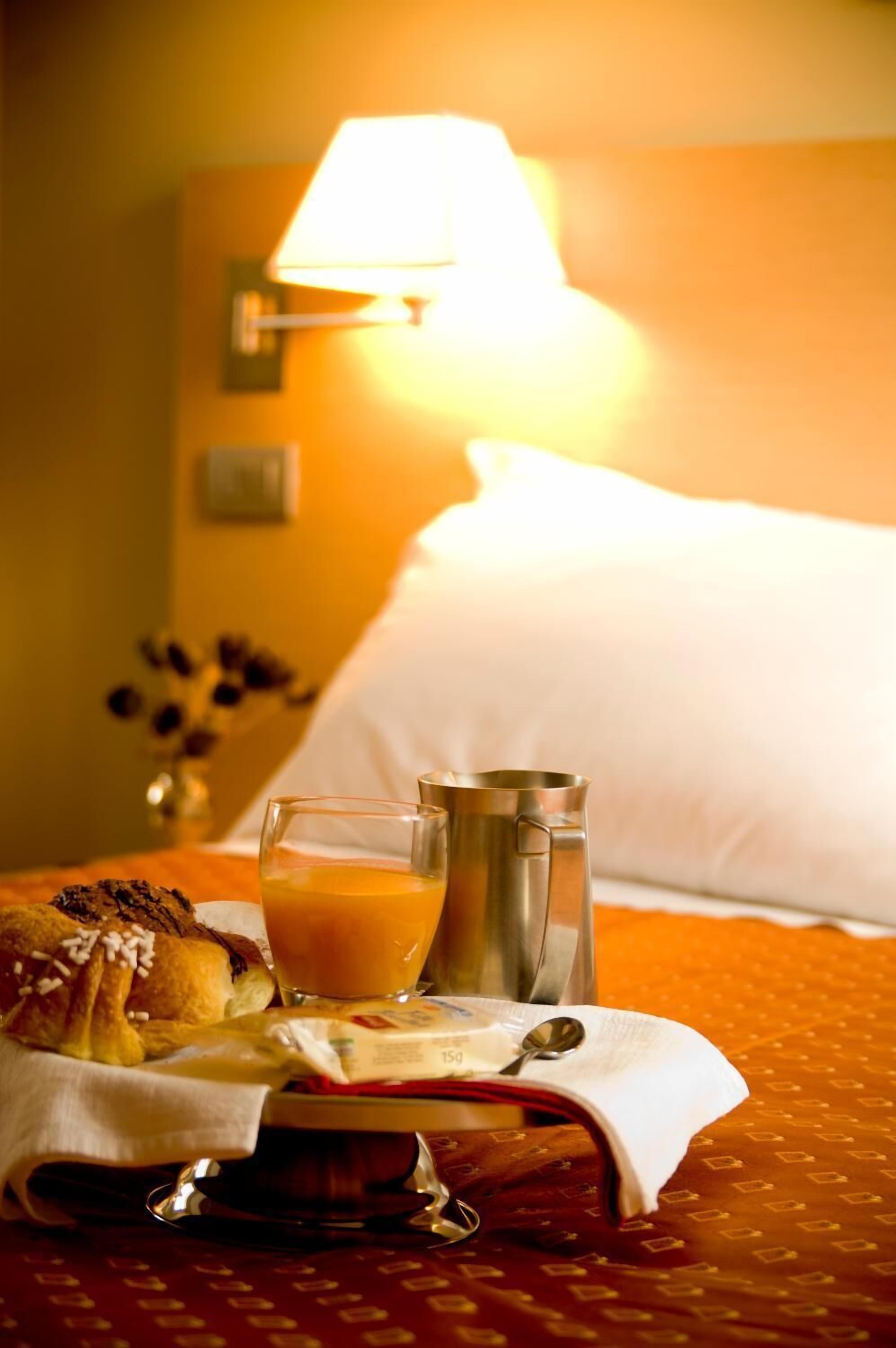 A breakfast setup with a croissant, orange juice, and a metal pitcher on a hotel bed.